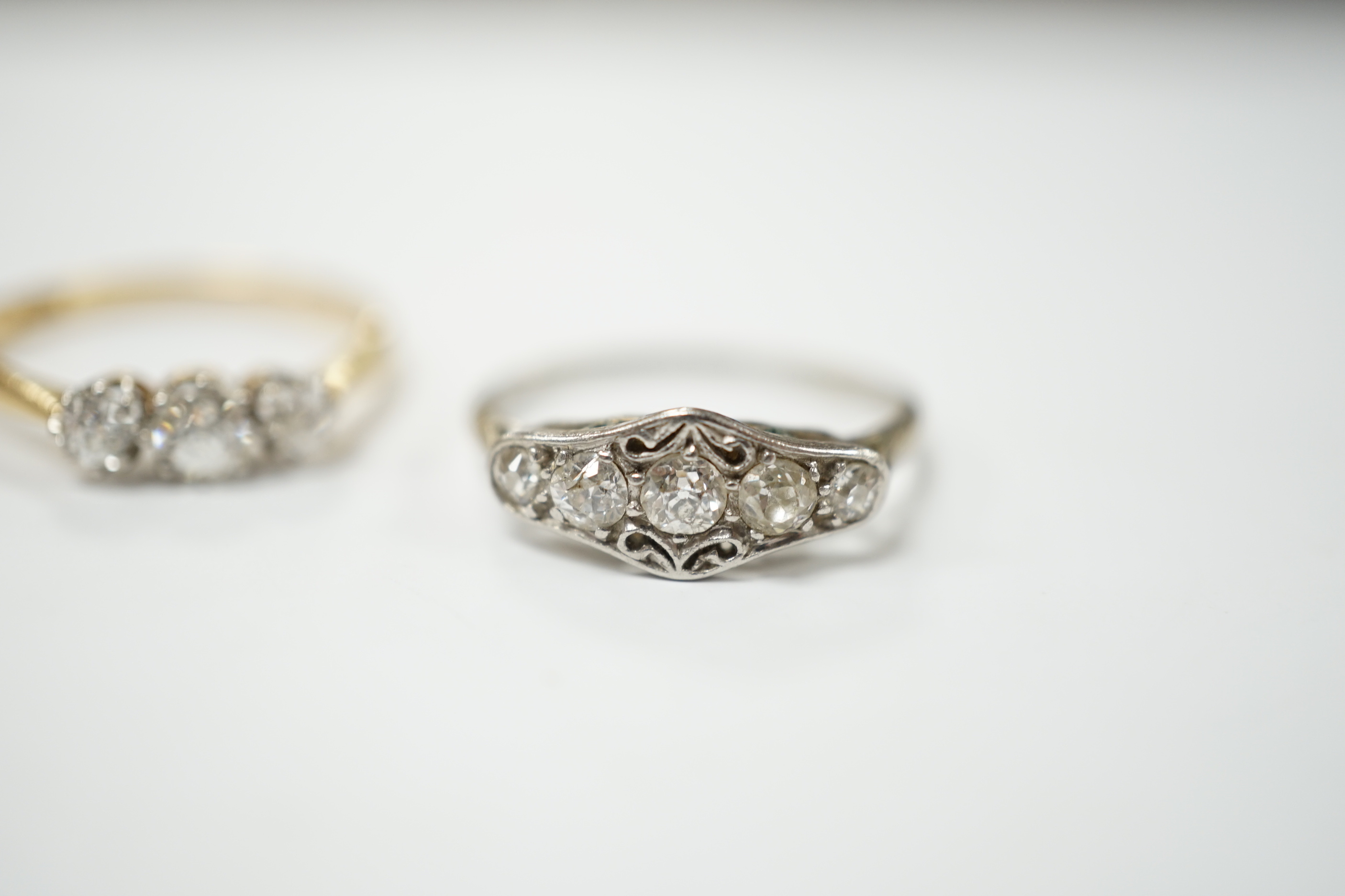 An 18ct gold three stone diamond ring, size M and a white metal five stone diamond dress ring, size M